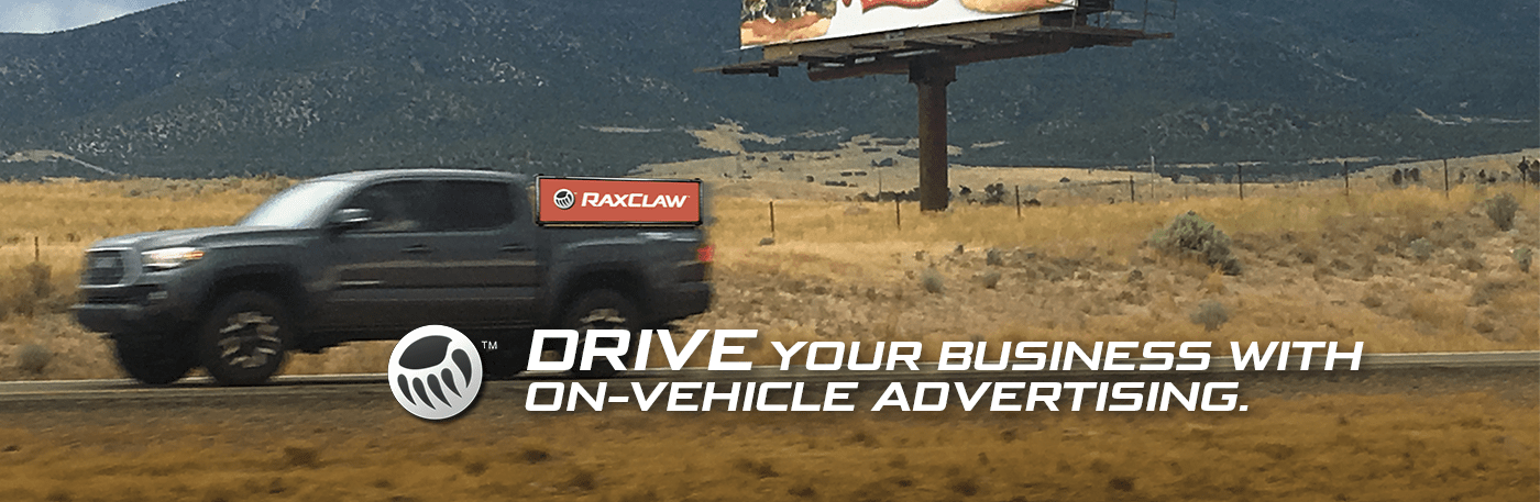 A gray pickup truck speeds along a rural highway with a promotional message about on-vehicle advertising in the foreground.